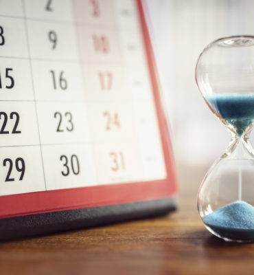Laufende Sanduhr steht vor einem Tischkalender